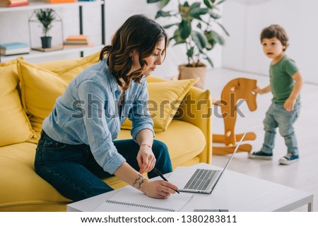 kid looking how mother working with laptop in living room Royalty-Free Stock Photo #1380283811