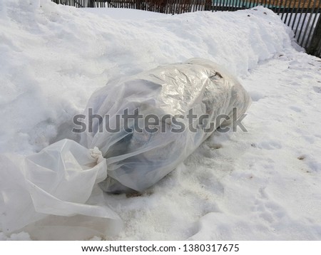 A large package of garbage lies right on the road against the backdrop of snow in winter or spring