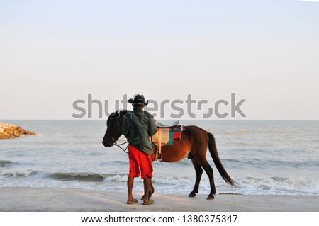 A man in cowboy hat standing with horse on the beach in evening