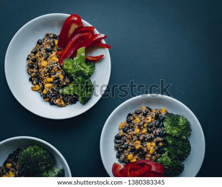 Vegan meal - Mexican style quinoa with black beans, sweetcorn, red bell pepper and broccoli presented in minimalistic manner on simple black background.