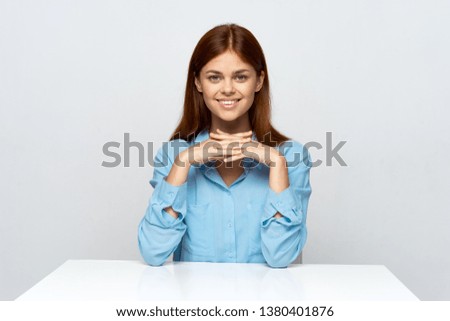 Smiling business woman in blue shirt is sitting at her desk against gray background
