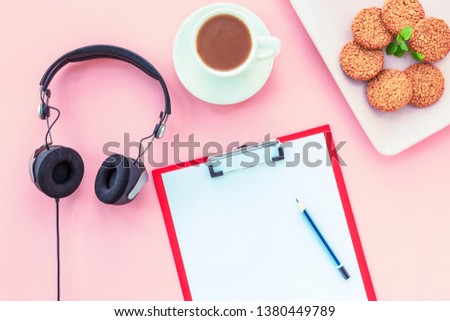 A cup of coffee, rice crackers, notebook with pencil and headphones on a pink background. Cosy workspace. Top view, flat lay.