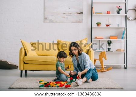 Mother and son playing on carpet in living room Royalty-Free Stock Photo #1380486806