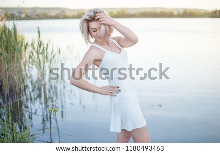 The girl in the white dress on the lake enjoys the summer.
