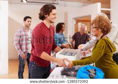 People Donating Food To Charity Food Bank Collection In Community Center Royalty-Free Stock Photo #1380573392