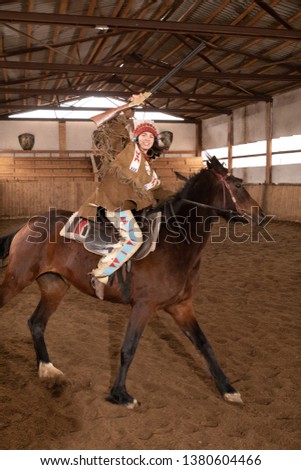 brunette girl in clothes and a headdress of a native americans riding a horse in a pen in an arena
