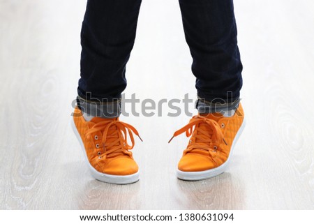 New orange sneakers with soft white soles closeup. Pigeon-toed foot position. Legs of a girl dressed in jeans in a clumsy pose on tiptoes isolated on light laminate. The first dance lesson of beginner