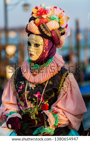 Young girl in a pink flower suit and a head dress with colorful flowers, and a mask at the carnival in Venice.