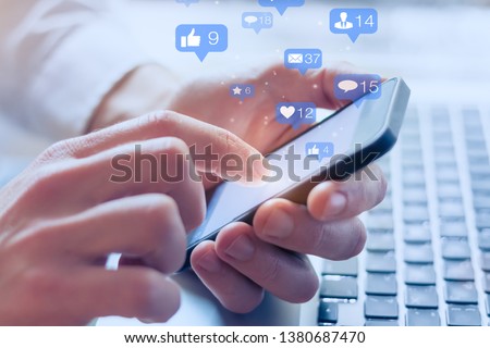 Social media interactions on mobile phone, concept with notification icons of like, message, email, comment and star above smartphone screen, person hands holding device, internet digital marketing Royalty-Free Stock Photo #1380687470
