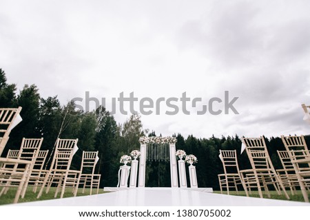 Very beautiful outside ceremony. classical wedding in forest. The arch is wooden. White flowers. White chairs. Rite. Bride and groom. Decor. Floristics. In the open air. Path from the petals of roses.
