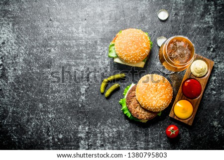 Burger with beer, sauces and gherkins. On black rustic background