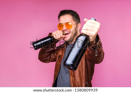 Photo of happy brunet man in orange glasses and leather jacket with two bottles in hands