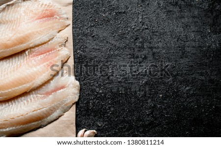Tilapia fish fillet on paper. On black rustic background