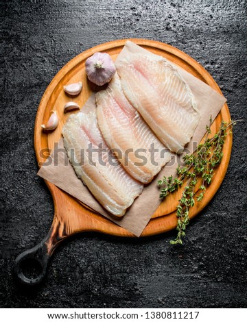 Fish fillet on paper on a round cutting Board with thyme and garlic cloves. On black rustic background