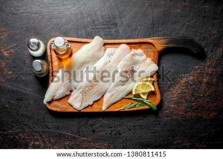 Fish fillet on a cutting Board with slices of lemon, oil and spices. On dark rustic background