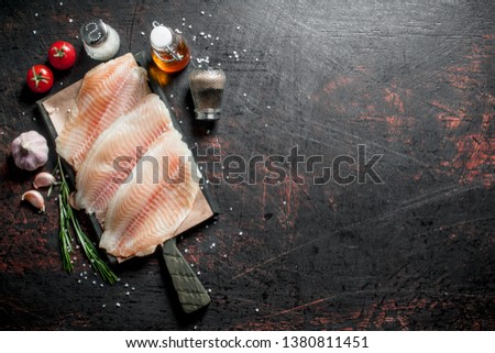Fish fillet on a cutting Board with spices, rosemary, garlic and oil. On dark rustic background