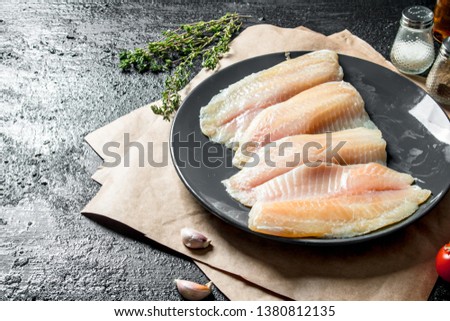 Fish fillet on plate with paper, thyme and garlic cloves. On black rustic background