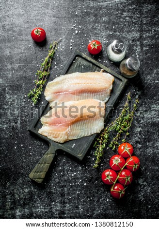 Fish fillet on a cutting Board with thyme, spices and tomatoes on a branch. On black rustic background