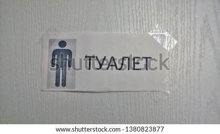 Texture, wallpaper, background, image of a white wooden door with the inscription "Toilet" pasted on the adhesive tape in Russian and an adjacent picture denoting a man.