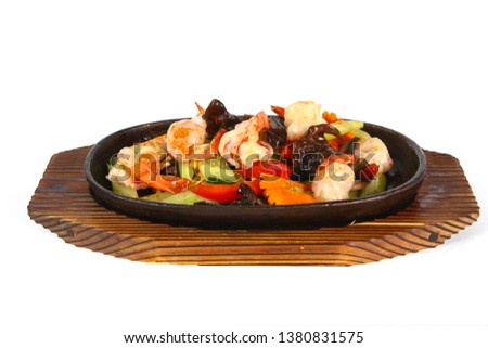 Meat baked in a cast iron pan with pieces of vegetables, Chinese cuisine, on a wooden Board on a light background.