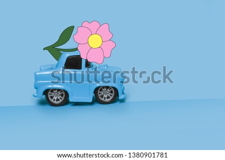 Blue retro toy car delivering a bouquet of flowers on a blue, heavenly background. Postcard February 14, Valentine's Day. Flower delivery. March 8, International Happy Women's Day
