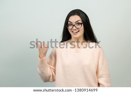 Happy young caucasian female in a pink jumper pointing fingers away, showing copy space for your text.