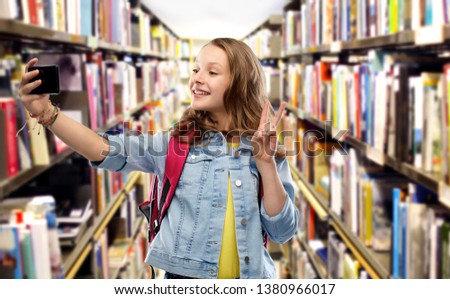 education, school and people concept - happy smiling teenage student girl with bag taking selfie by smartphone and showing peace over library background