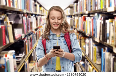 education, school and people concept - happy smiling teenage student girl with bag and smartphone over library background