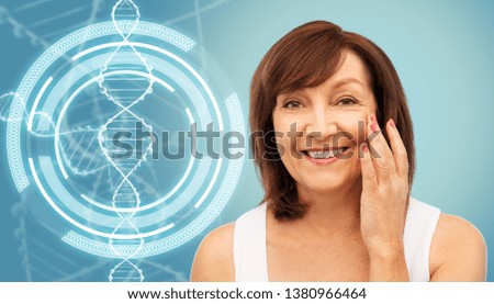 beauty, biotechnology and anti-age concept - portrait of smiling senior woman touching her face over blue background and dna molecule hologram Royalty-Free Stock Photo #1380966464