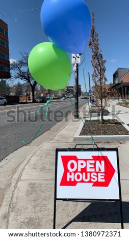 Open House sign with green and blue balloons next to city street