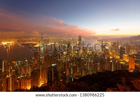 Scenery of Hong Kong at dawn, viewed from top of Victoria Peak, with a skyline of crowded skyscrapers by the Harbour & in Kowloon Downtown across the seaport and city lights under dramatic dawning sky