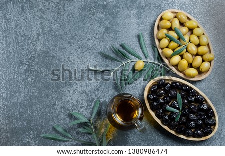 Glass bottle of homemade olive oil and olive tree branch, raw turkish green and black olive seeds and leaves on grey rustic table. olives background, olivae oleum Royalty-Free Stock Photo #1380986474