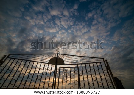 Iron gate with a cross on the background of a cloudy sky.