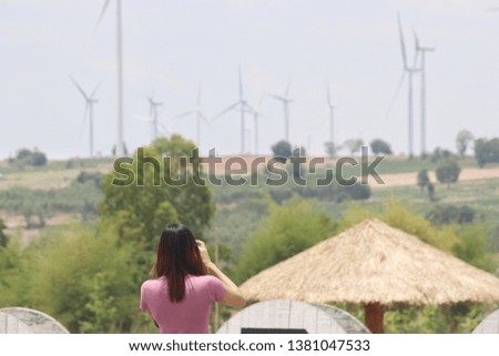 women  take  photograph with blurred Wind turbine electric power farm background  during  travel at saraburi thailand