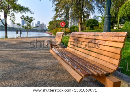 Wooden bench, no bikes allowed sign and lamp post at the park in Bangkok, Thailand with lake, trees and city view.