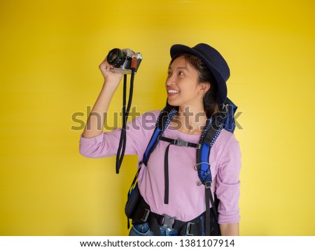 Searching for inspiring places. smiling adventure tourist woman with backpack and film camera taking photo isolated on yellow