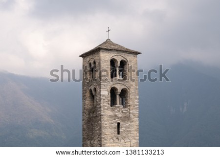 Romanesque bell tower with mountains - the Alps - in the background. Fog and mist.
