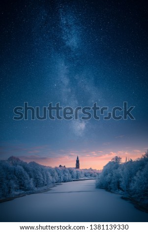 Majestic milky way over a clock tower and icy river at winter
