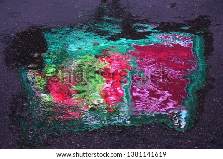 Multicolor wet spot is on rainy asphalt. Reflection from billbord.