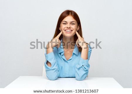 A woman sits at the table and holds her fingers near the cheeks                        