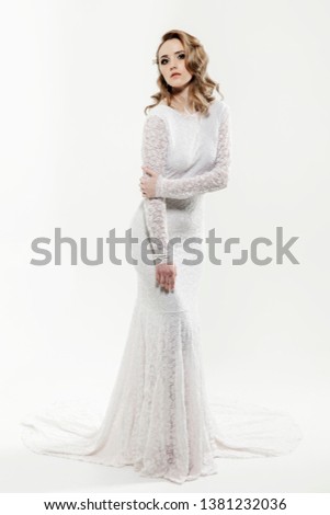 Beautiful girl with blond hair posing. The bride in a beautiful dress with a long train on a white background.