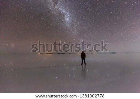 Man standing under night sky and milky way reflections on the salar de Uyuni 