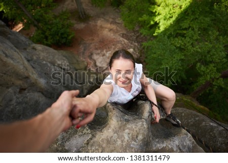 Happy woman climbing rock, friend helping her getting up to the top with hand helping. Teamwork and outdoors summer activities concept for risky people. Top view and beautiful nature on background. Royalty-Free Stock Photo #1381311479