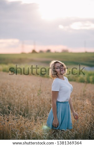 Beautiful Girl in a field at sunset. Woman with arms outstretched in a wheat field. Young woman in summer dress standing in the field with raised arms.  Young woman enjoying nature.