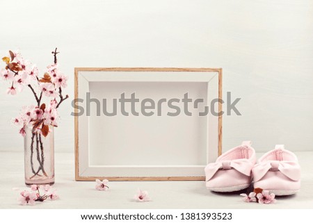 Mock up with empty picture frame, pink tender spring flowers and small baby girl shoes. Baby shower, girl birthday concept
