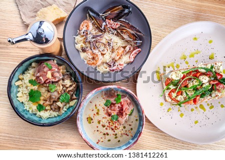 Top view on served food on white wooden table. Italian cuisine bruschetta, jamon cream soup, risotto and seafood pasta for lunch. Copy space for design. Picture for menu, recipe