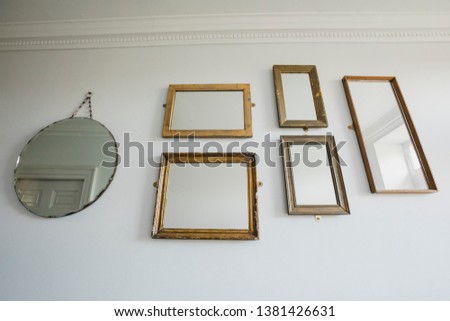 Low angle view of a wall in a house which has a variety of different shaped mirrors hanging on the wall.