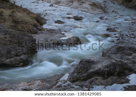 A flowing water in a rocky forest area. Due to long exposure, the water is partial intentionally blurred, looking smooth and fluffy. No persons. Stones, grass and little rocks in the environment.