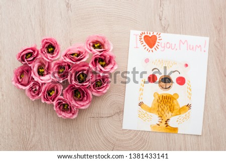 top view of heart sign made of eustoma flowers and card with i love you mom lettering on wooden surface