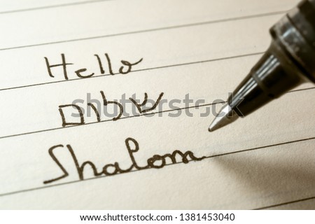 Beginner Hebrew language learner writing Hello Shalom word in Hebrew alphabet on a notebook close-up shot Royalty-Free Stock Photo #1381453040